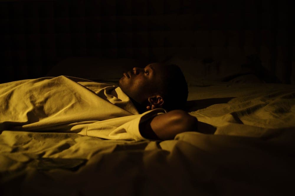 Person asleep in a dark bedroom, face turned toward the pillow