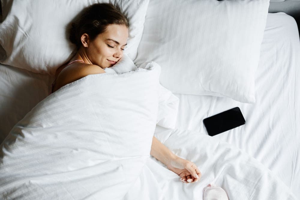 Person sleeping on their back under white bedding
