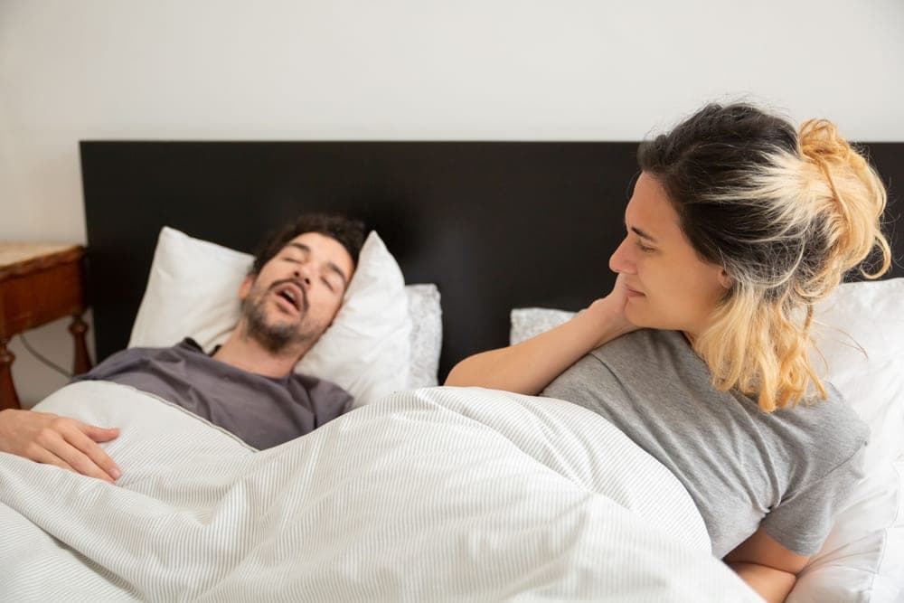 Empty pillow beside a sleeping partner in a dark bedroom