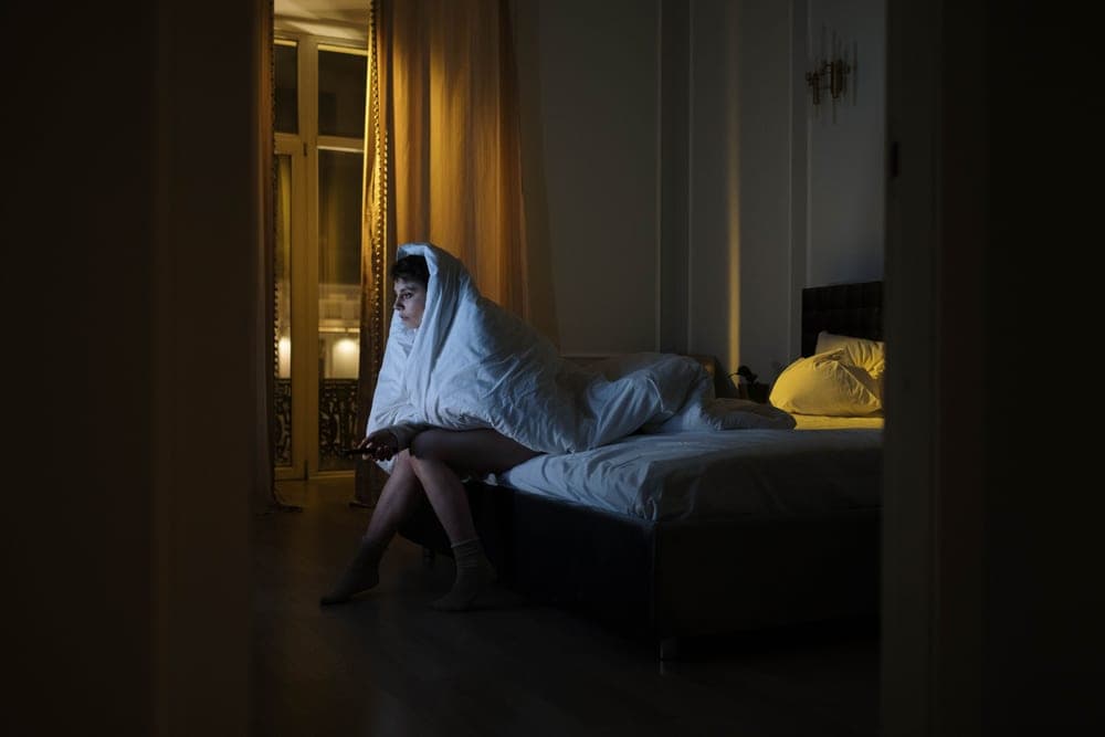 Exhausted person sitting on the edge of a bed at night