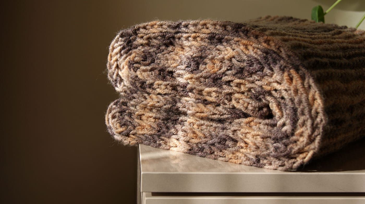 Chunky knit blanket folded across the end of a made bed - illustrative category image