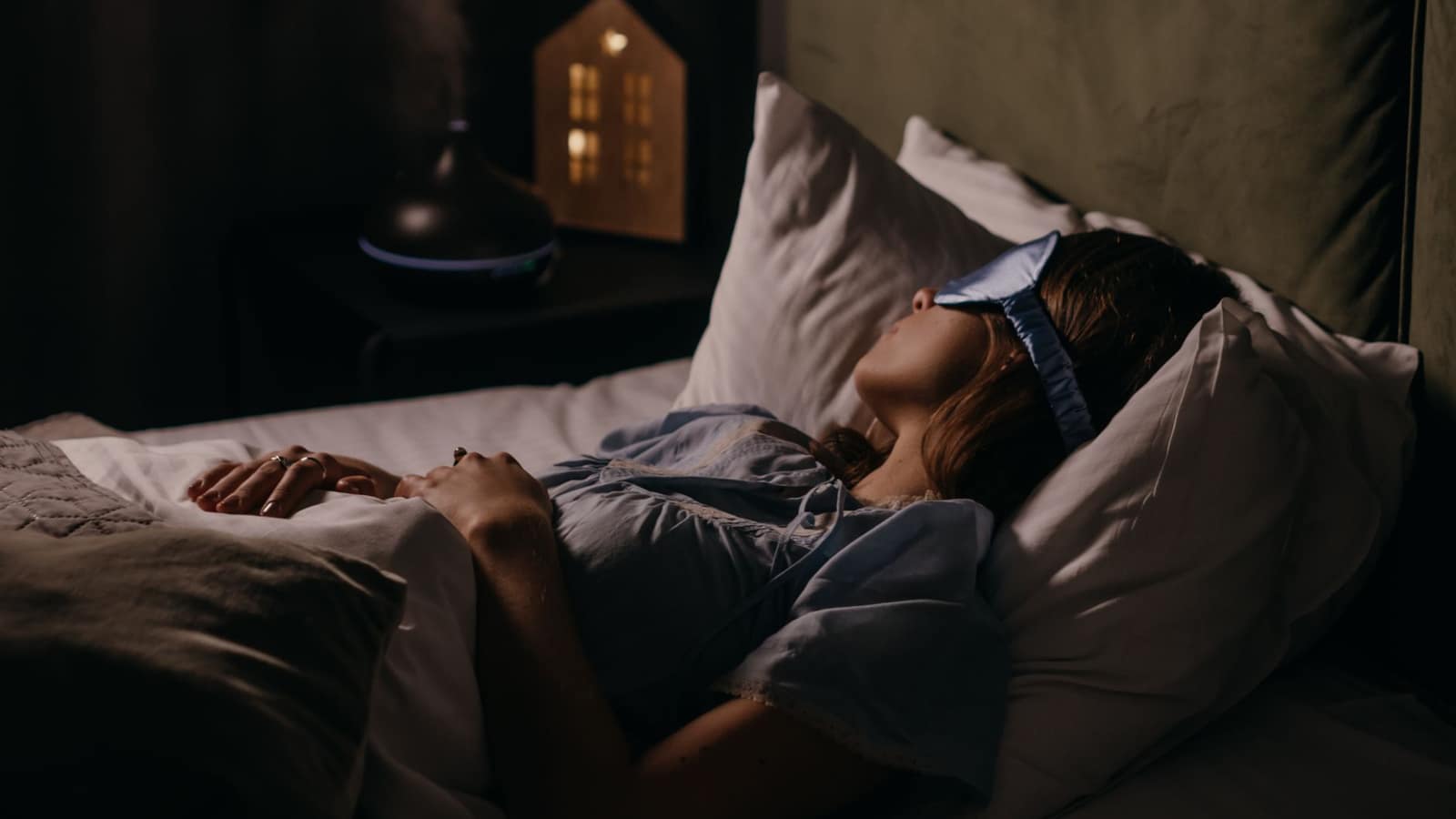 Person asleep in a dim bedroom with bedding pulled up