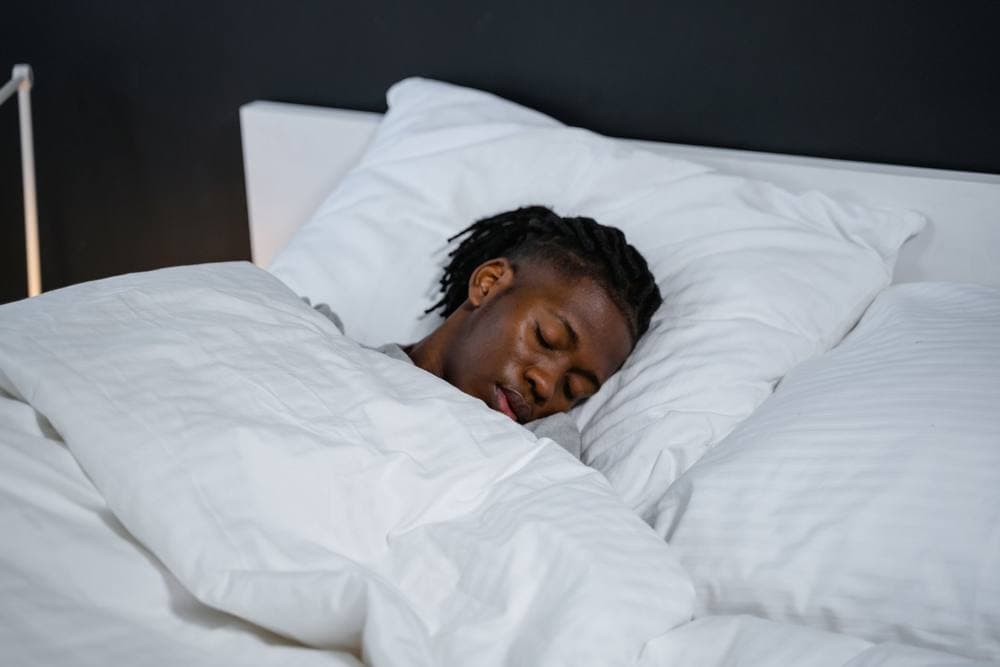 Man sleeping in bed with white sheets in a darkened room
