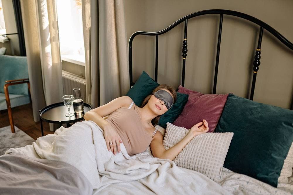 Woman asleep in bed wearing an eye mask among soft pillows
