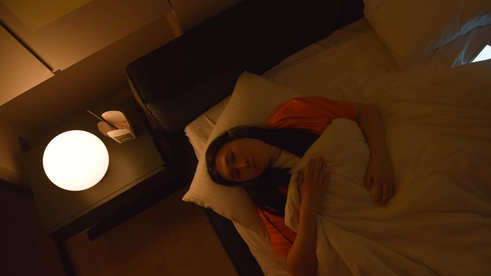 Person asleep on their side in a dark bedroom wearing a soft head covering