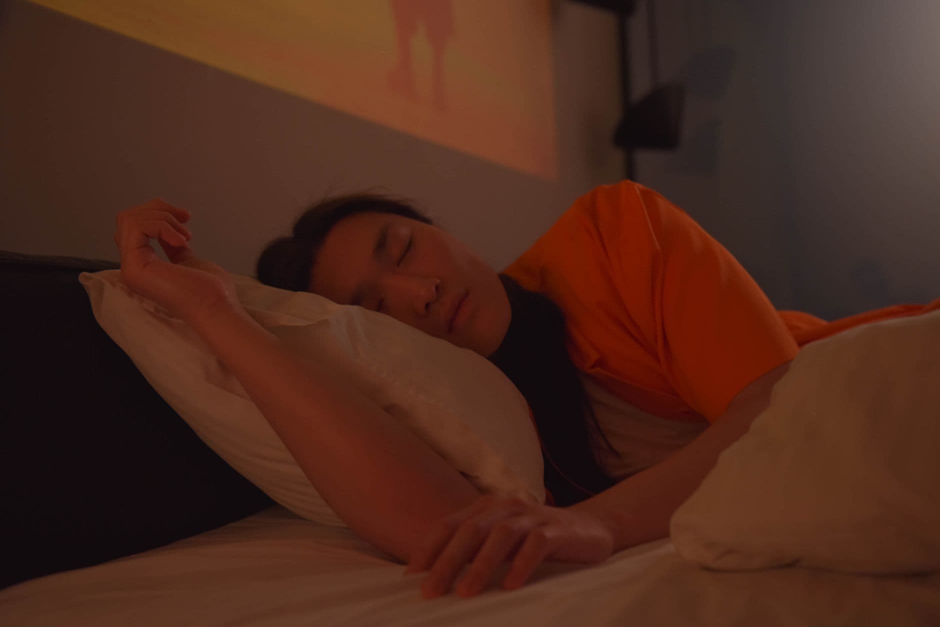 Person asleep on their side in a dim bedroom with soft light falling behind them