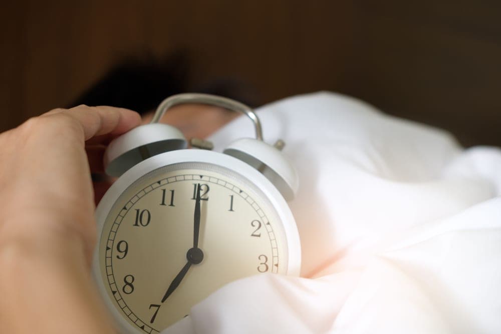 Close-up of a hand pressing the snooze button on a bedside alarm clock