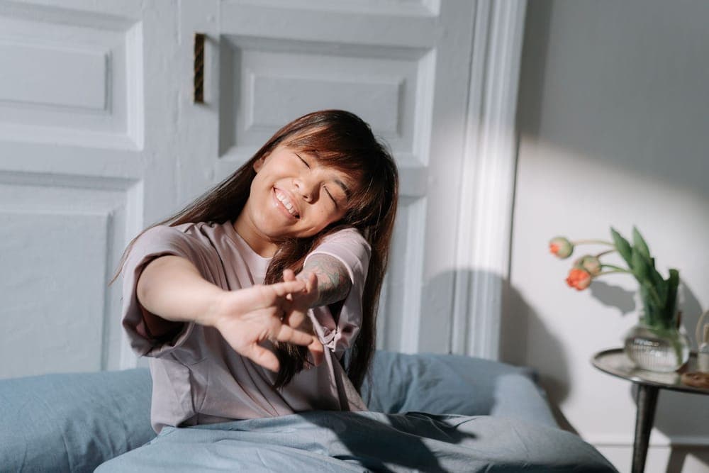 Person stretching awake in bed as morning light comes through a window