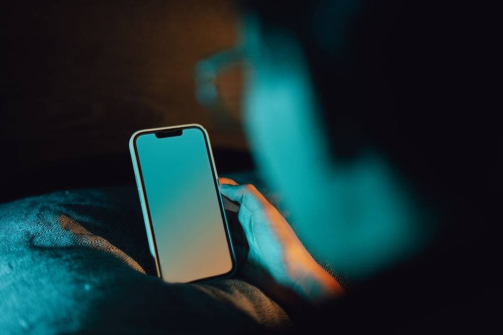 Hand holding a smartphone in a dark bedroom