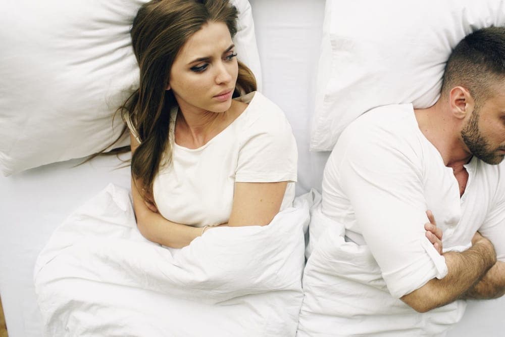 Couple lying back to back in bed at night, one of them awake