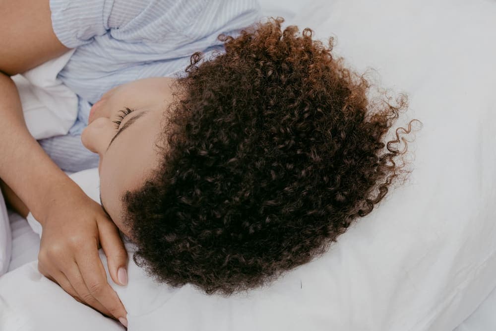 Person asleep on their side with their ear against a pillow in a dim bedroom