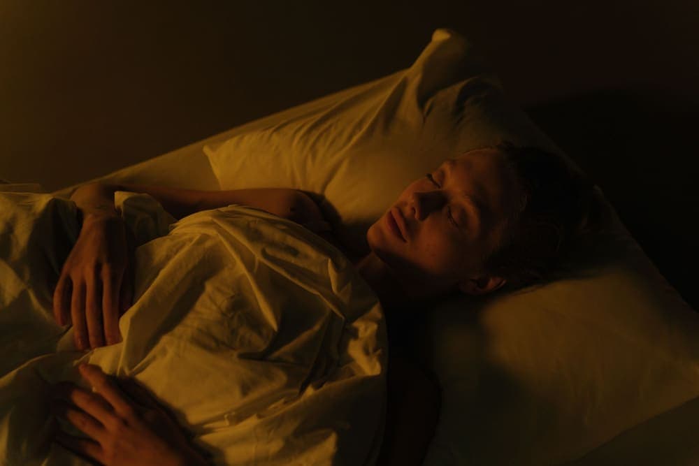 Person asleep in a dimly lit bedroom wrapped in a white blanket - illustrative category image
