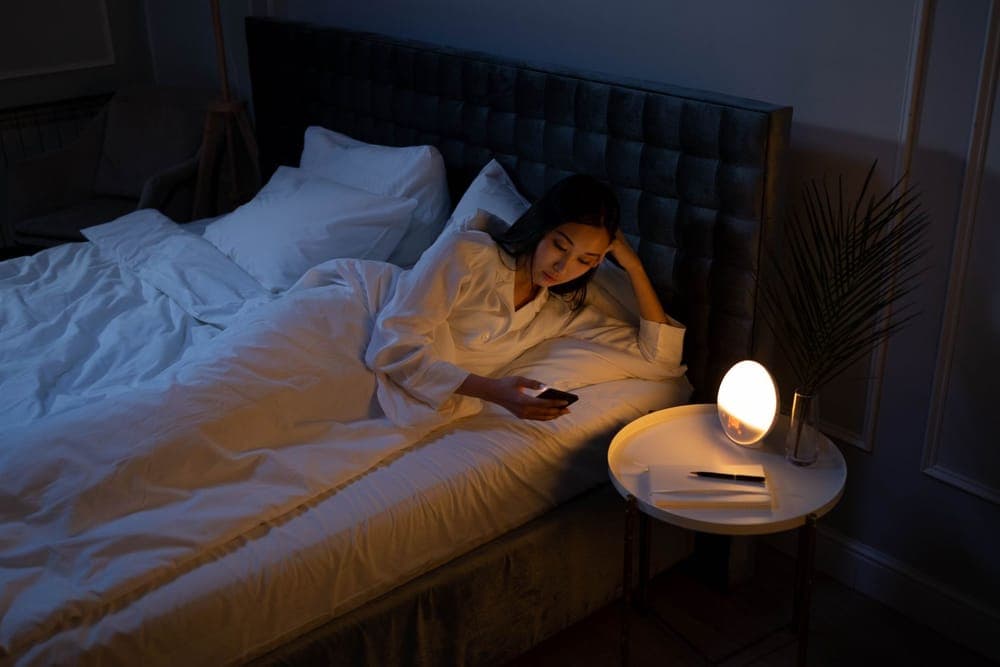 Person in bed at night with a phone on the nightstand beside them