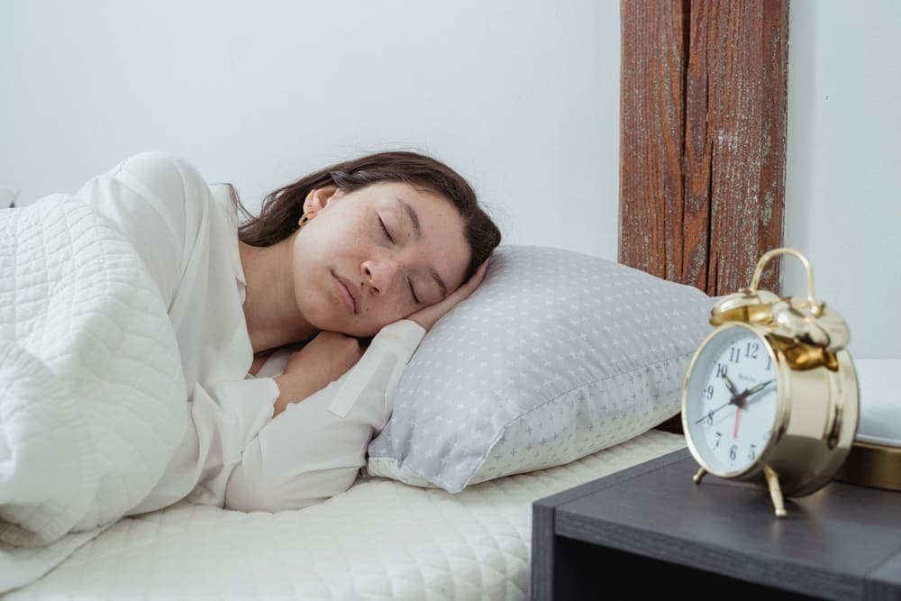 Person asleep on their side with a hand under their head on a white pillow - illustrative category image