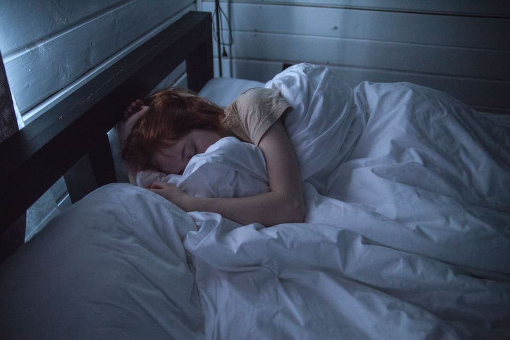 Person asleep under white sheets in a softly lit bedroom - illustrative category image