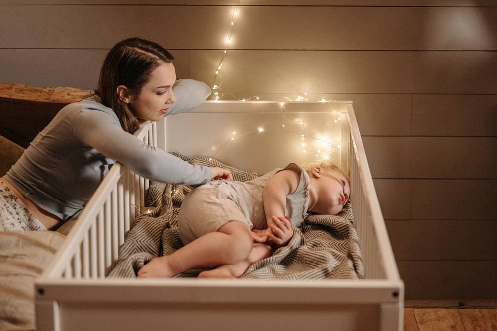 Warmly lit bedroom with a parent beside a sleeping baby