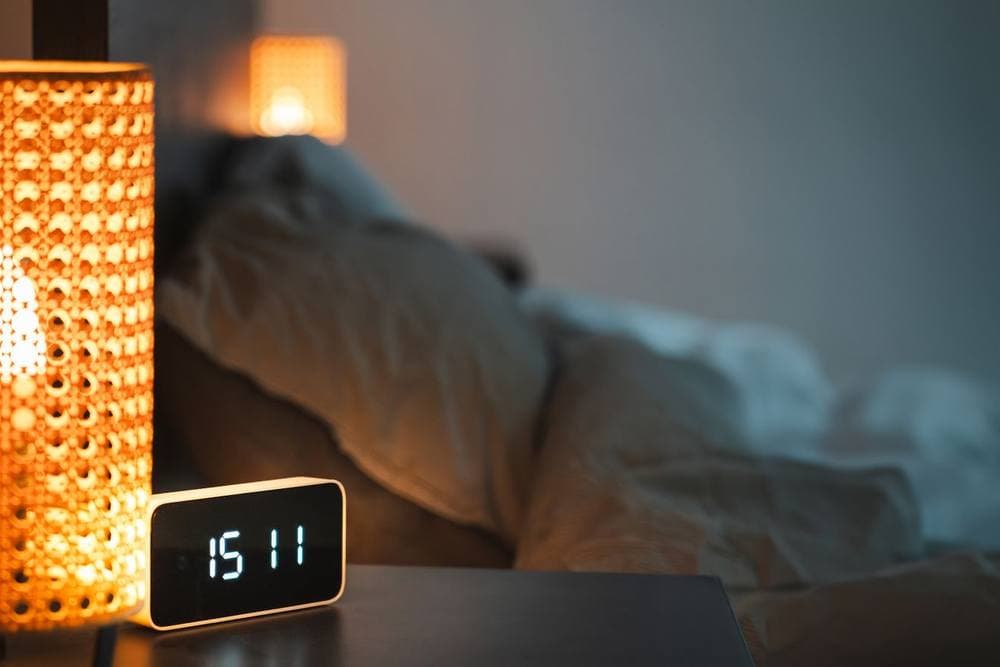 Bedroom at night with a glowing lamp and a digital alarm clock - illustrative category image