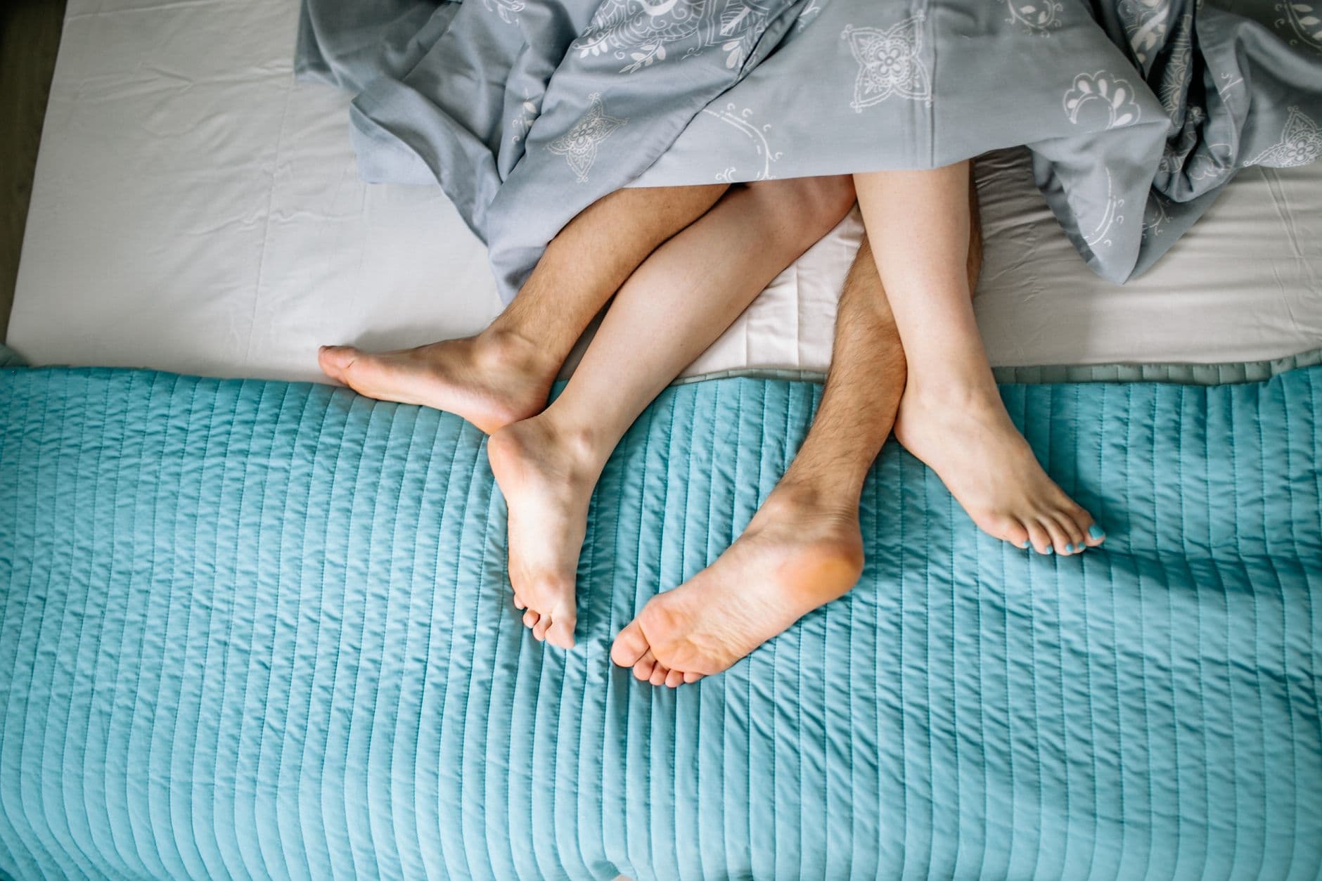 Two people asleep under a single shared blanket, seen from above