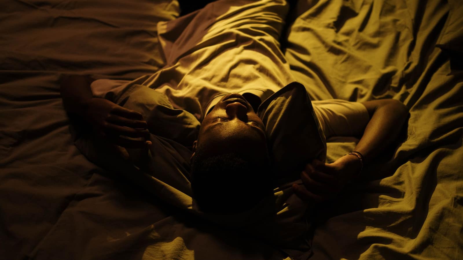 Feet and lower legs under a rumpled blanket on an unmade bed at night