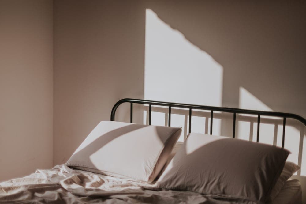 Neatly made bed with a plain comforter in morning light