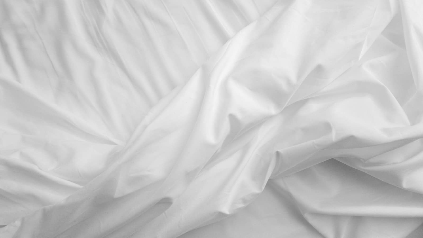 Tightly made bed with smooth, taut white sheets in daylight